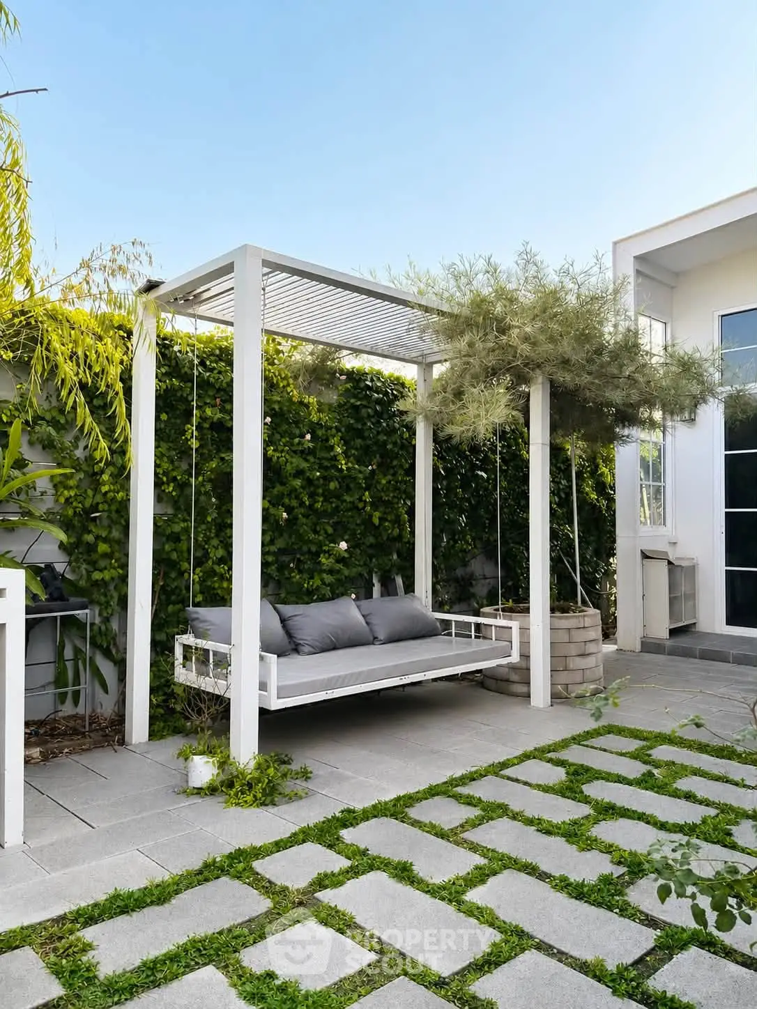 Charming outdoor patio with modern swing and lush greenery, perfect for relaxation and entertaining.