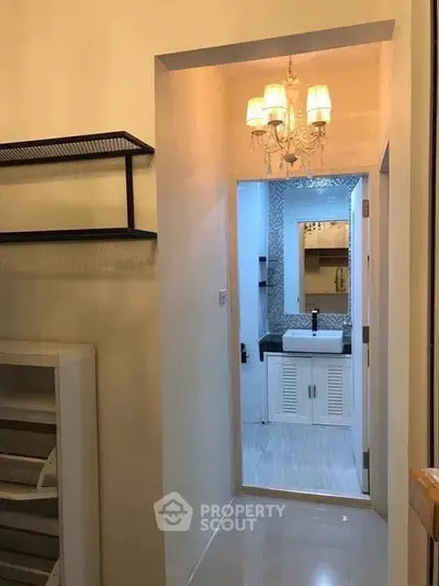 Chic hallway leading to a modern bathroom with elegant chandelier lighting.