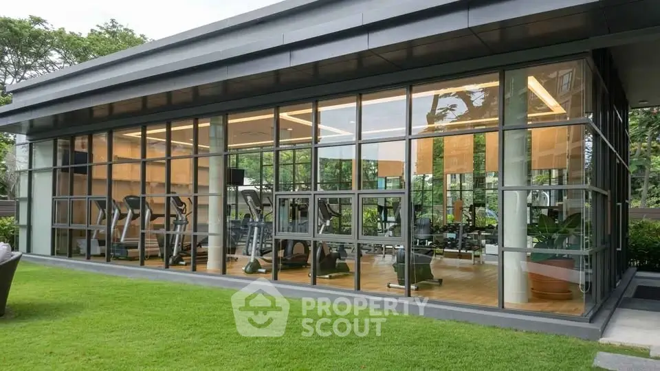 Modern glass-walled gym with lush green surroundings in a luxury residential complex.