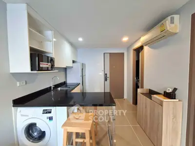 Modern kitchen with sleek black countertops, washing machine, and microwave in a stylish apartment.