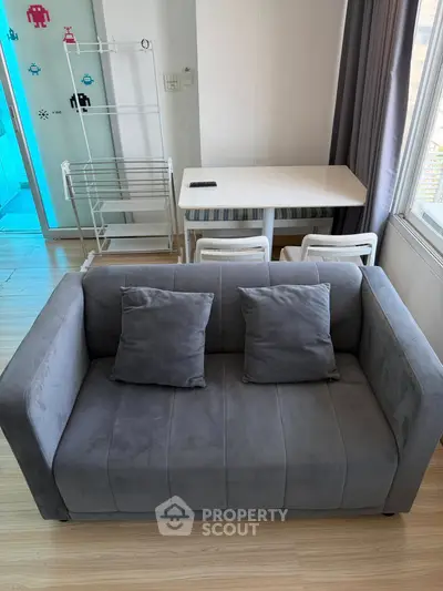 Modern living room with stylish gray sofa and dining area, featuring bright natural light and contemporary decor.
