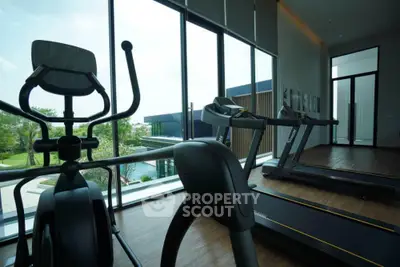Modern gym with large windows overlooking lush greenery and pool area.