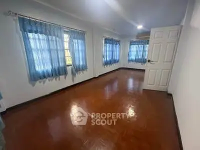 Spacious empty room with wooden flooring and blue curtains, ideal for customization.