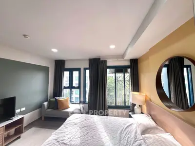 Modern bedroom with large windows, stylish decor, and cozy seating area in a bright apartment.