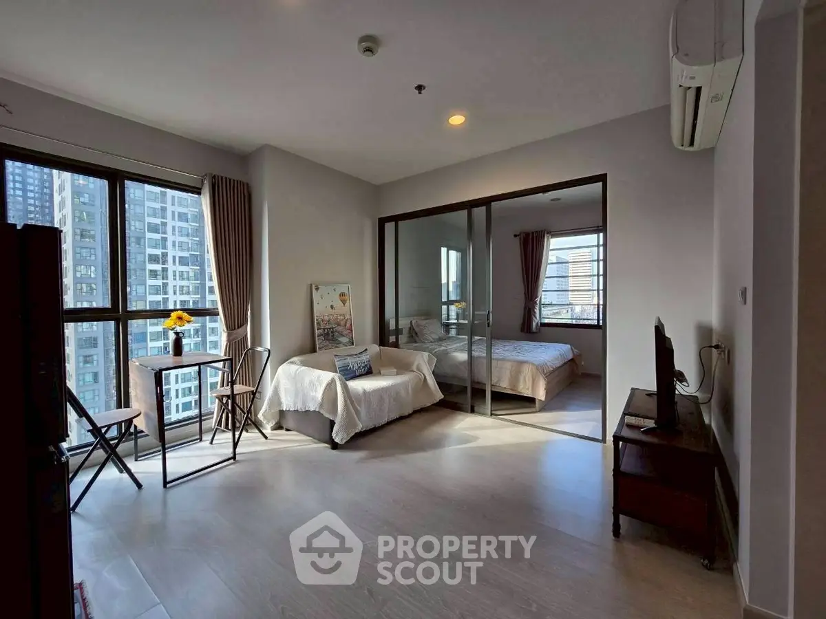 Modern apartment with open living room and bedroom, featuring large windows and city views.