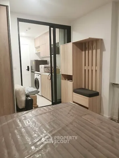 Modern studio apartment with compact kitchen and washing machine, featuring sleek wooden cabinetry and cozy seating area.