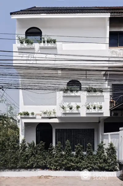 Charming white three-story townhouse with lush greenery and modern design.