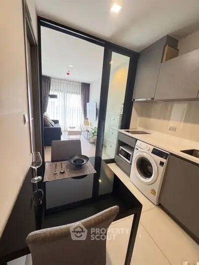 Modern apartment with sleek kitchen and cozy living area, featuring a washing machine and elegant dining setup.