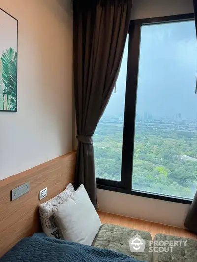 Cozy bedroom with a breathtaking panoramic view of the city skyline and lush greenery, featuring floor-to-ceiling windows and elegant dark curtains.