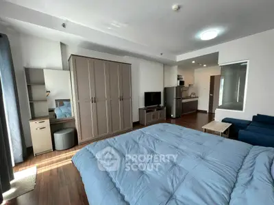 Spacious modern bedroom with cozy blue bedding and stylish furniture in a well-lit apartment.