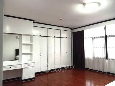Spacious bedroom with elegant built-in wardrobe and vanity, featuring polished wooden floors and ample natural light.