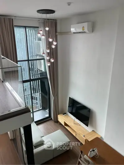 Modern loft-style living room with high ceiling and large windows offering city views.