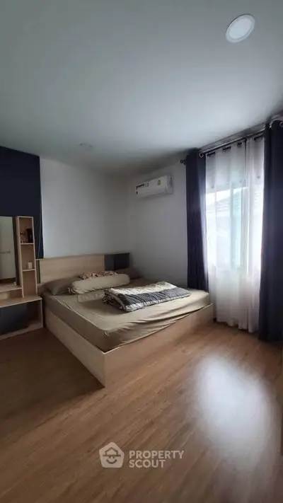 Cozy bedroom with wooden flooring and natural light through large window.