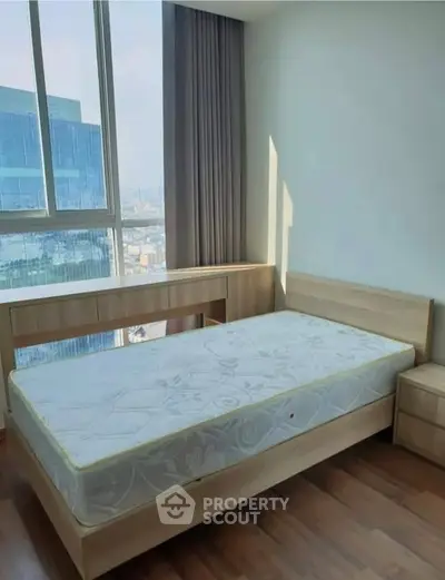 Bright bedroom with large window and city view, featuring wooden furniture and a comfortable mattress.