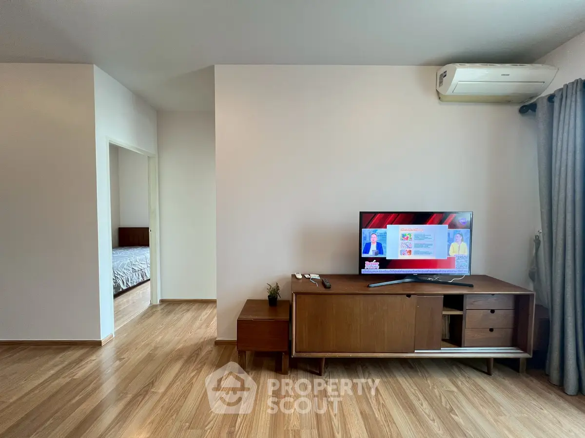 Modern living room with wooden flooring, TV unit, and air conditioning, leading to a cozy bedroom.