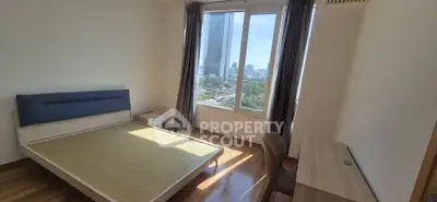 Bright bedroom with large window offering city view, wooden flooring, and modern furniture.