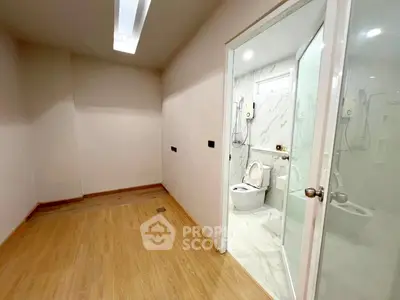 Modern bathroom with wooden flooring and glass door, featuring a sleek toilet and shower area.
