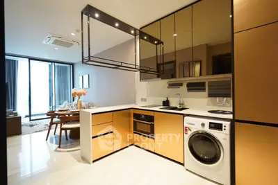 Modern kitchen with sleek design, featuring built-in oven and washing machine, open layout to dining area.
