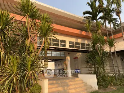 Modern building entrance with tropical landscaping and sleek architectural design.
