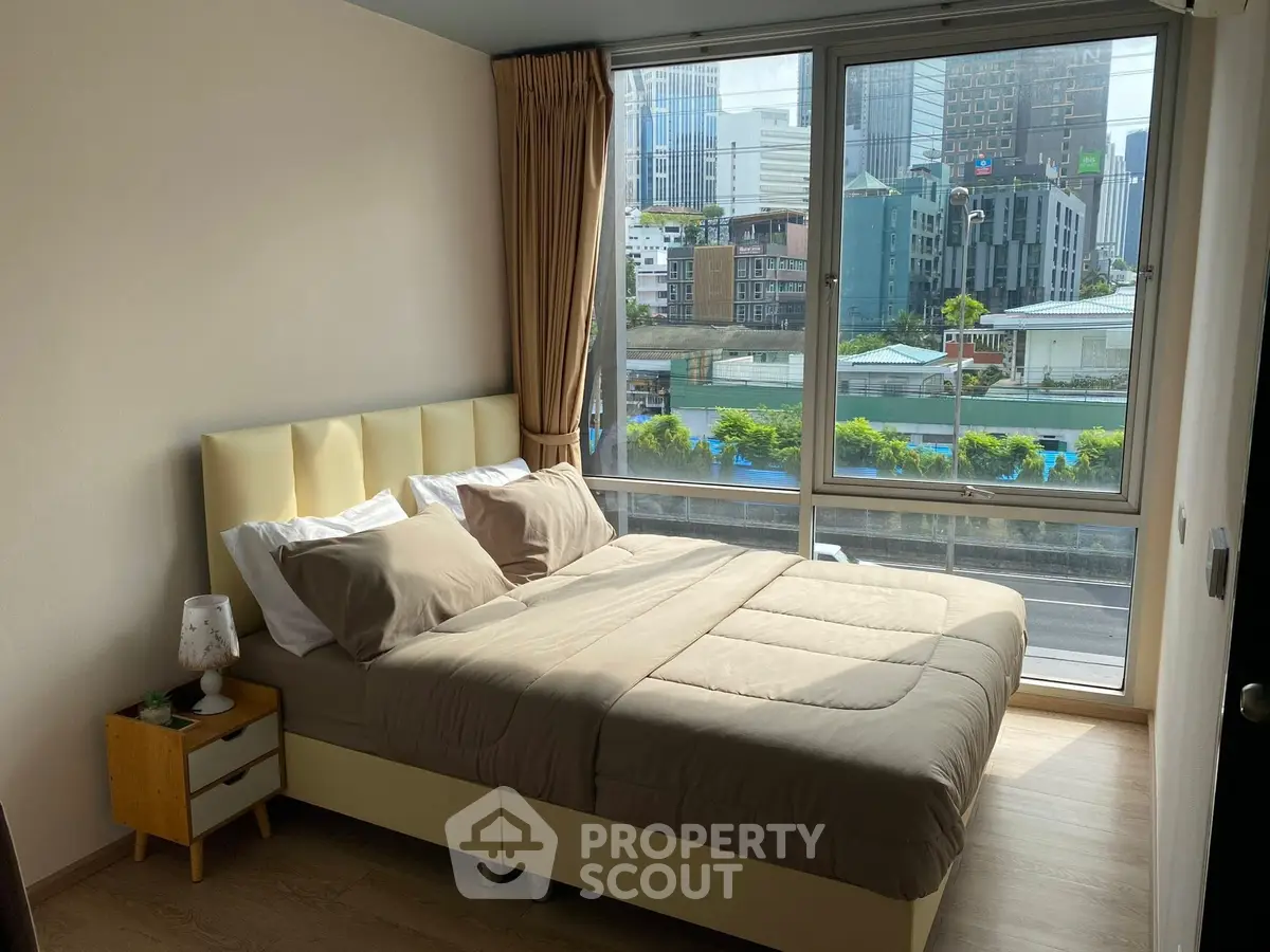 Modern bedroom with large window offering stunning city view, featuring cozy bed and stylish decor.