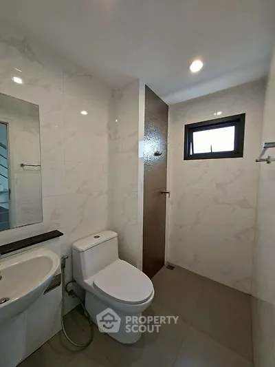 Modern bathroom with sleek fixtures and marble tiles, featuring a toilet and sink under recessed lighting.
