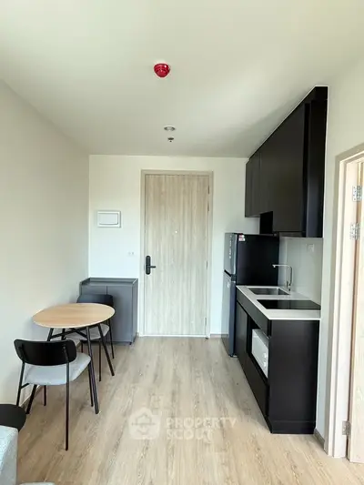 Modern compact kitchen with sleek black cabinets and dining area in a stylish apartment.