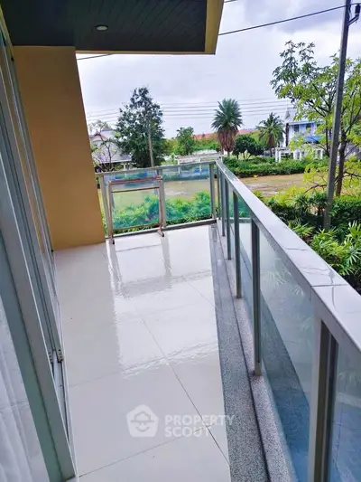 Spacious balcony with glass railing offering serene garden views in modern apartment.
