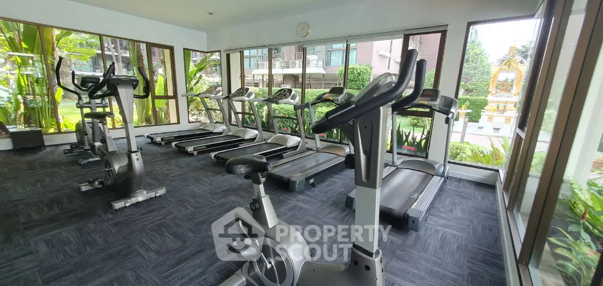 Modern gym with exercise equipment and large windows overlooking greenery.