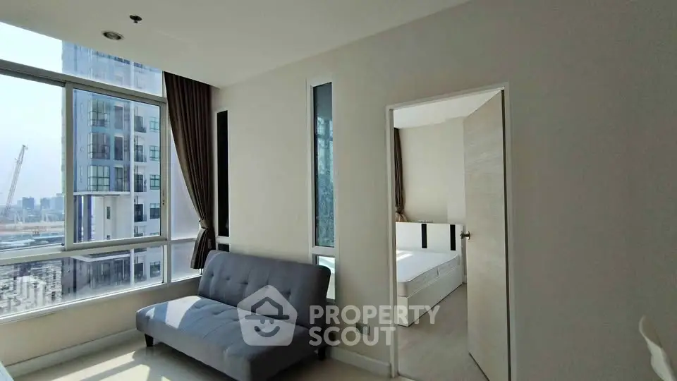 Modern apartment with large windows and natural light, featuring a cozy living area and adjacent bedroom.