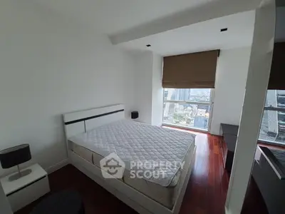 Spacious bedroom with large window offering city views, featuring modern furniture and hardwood floors.