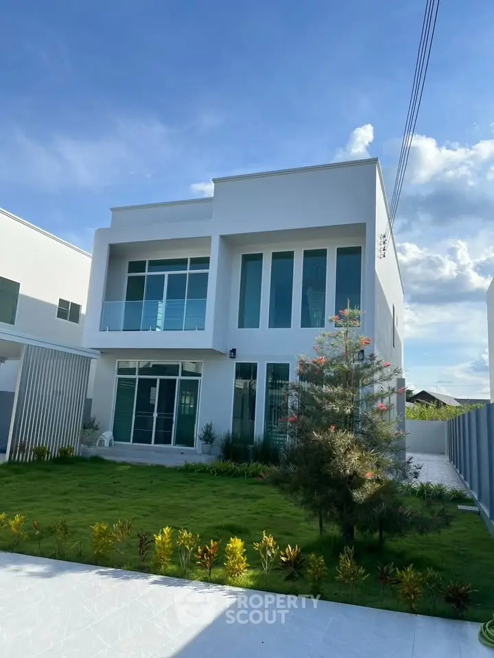 Modern two-story white house with large windows and lush green garden under a clear blue sky.