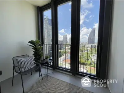 Sunlit balcony with a modern chair and lush plant, offering a stunning cityscape view, perfect for relaxation and urban living.