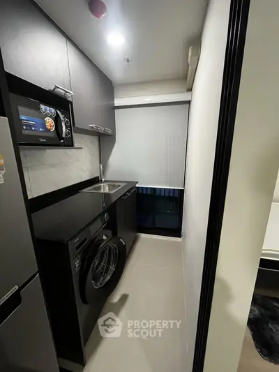 Modern compact kitchen with sleek appliances and washing machine in stylish apartment.