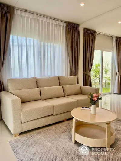 Elegant living room with beige sofa, round coffee table, and large windows with curtains.