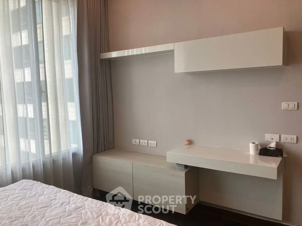 Modern bedroom with sleek built-in storage and large window for natural light.