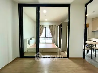 Modern bedroom with large mirror and wooden flooring, featuring a bright window view.