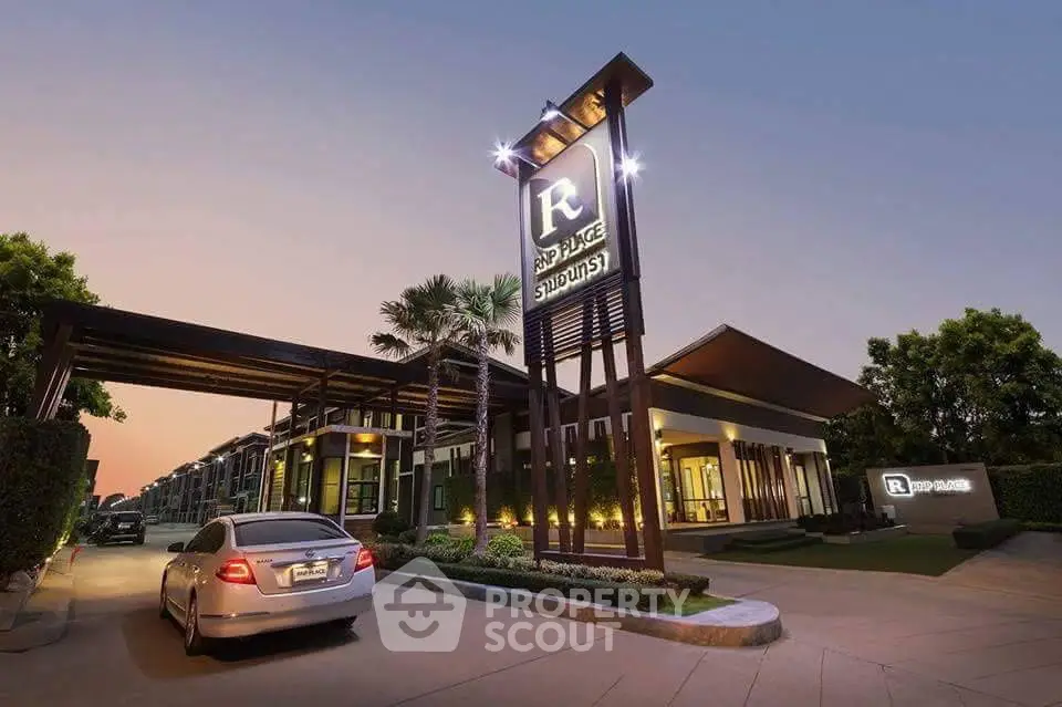 Modern residential complex entrance with sleek design and luxury car at sunset.