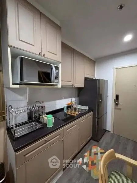 Modern kitchen with sleek cabinets, microwave, and stainless steel fridge in cozy apartment.