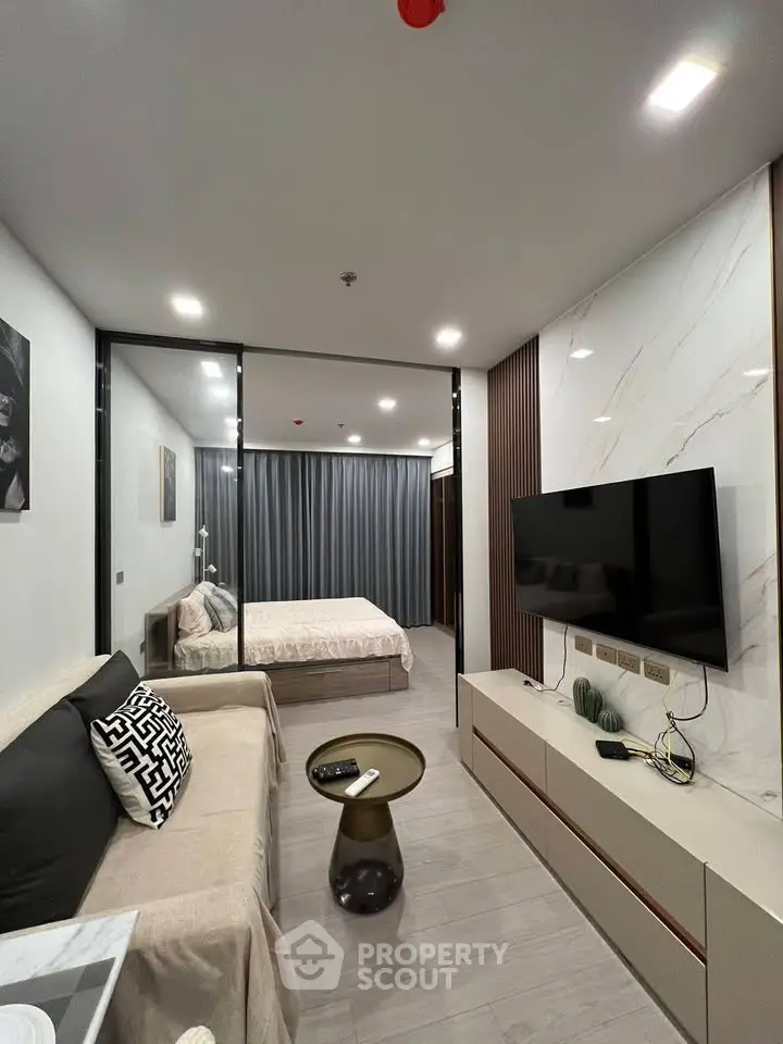 Modern studio apartment with sleek design, featuring a cozy living area and stylish bedroom separated by glass partition.