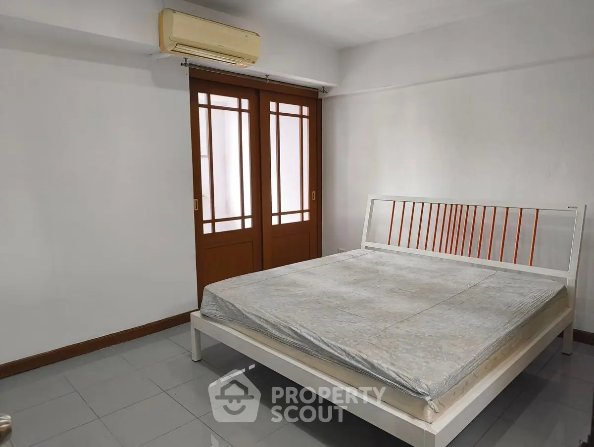 Spacious bedroom with minimalist design and large bed, featuring wooden sliding doors and air conditioning.