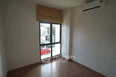 Bright empty room with wooden flooring and large window, perfect for customization.