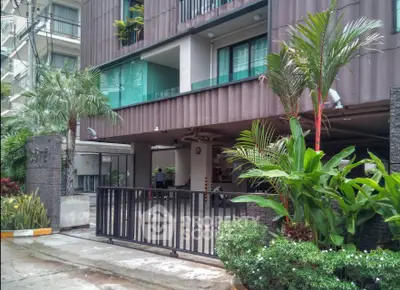 Modern apartment building entrance with lush greenery and secure gated access.