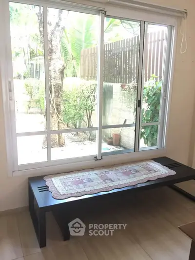 Bright interior with large window and garden view, featuring a stylish bench and wooden flooring.