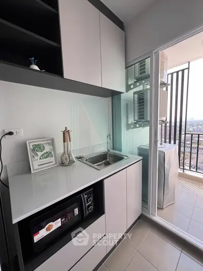 Modern kitchen with sleek cabinetry and balcony view, featuring microwave and washing machine.