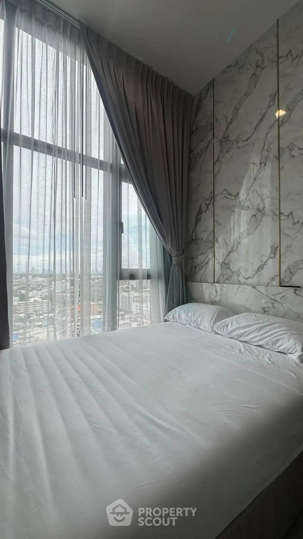 Luxurious bedroom with marble accent wall and floor-to-ceiling windows offering stunning city views.