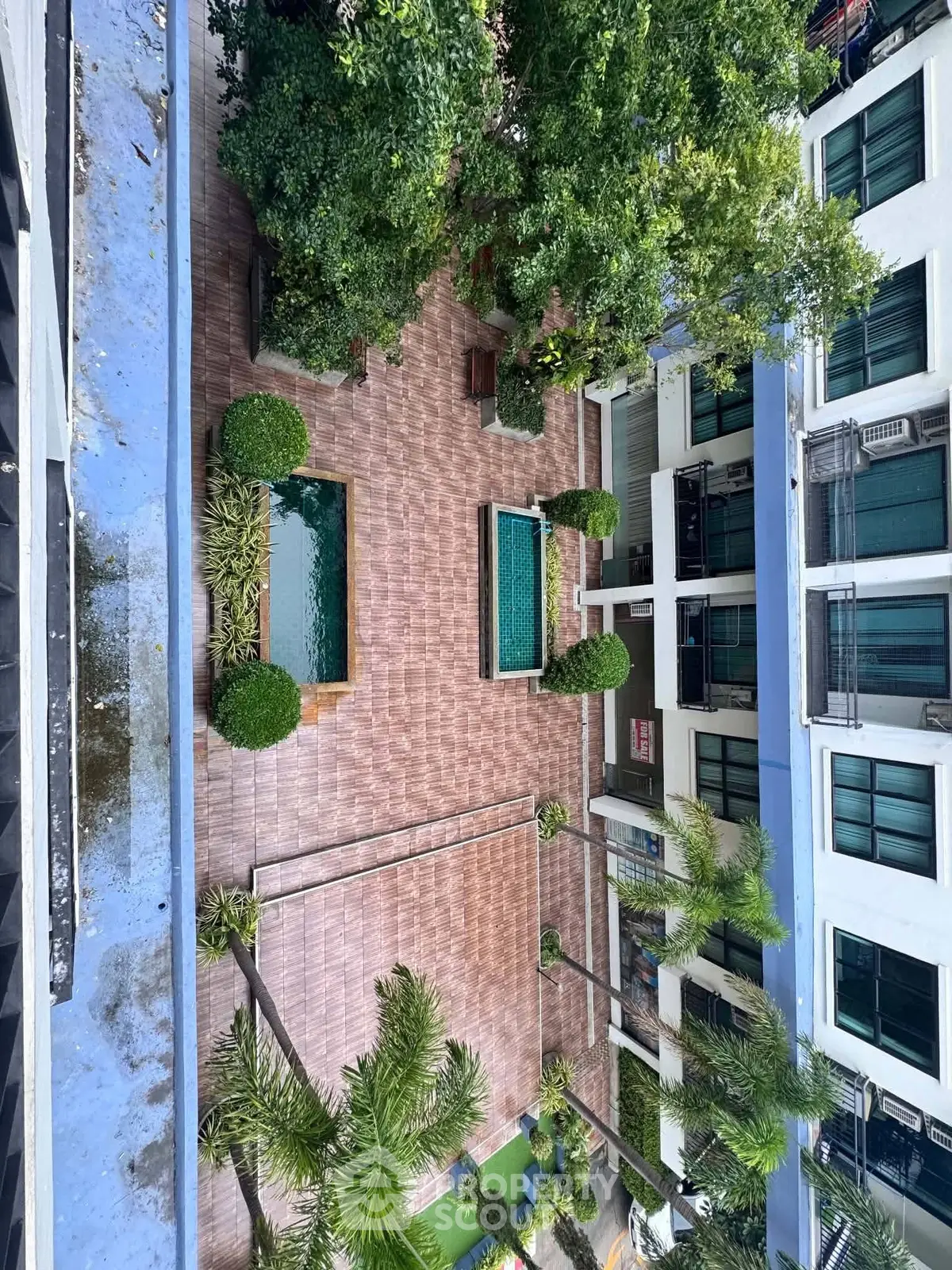 Stunning aerial view of a modern apartment complex with lush garden and pool area, perfect for urban living.