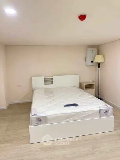 Modern minimalist bedroom with white bed and wooden flooring, ideal for cozy living.