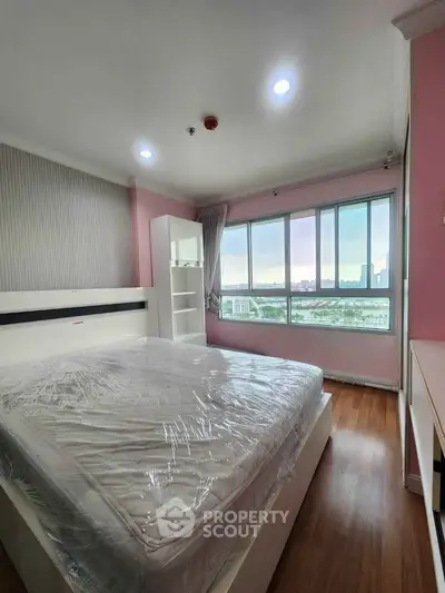 Spacious bedroom with large window offering stunning city view, modern furnishings, and wooden flooring.