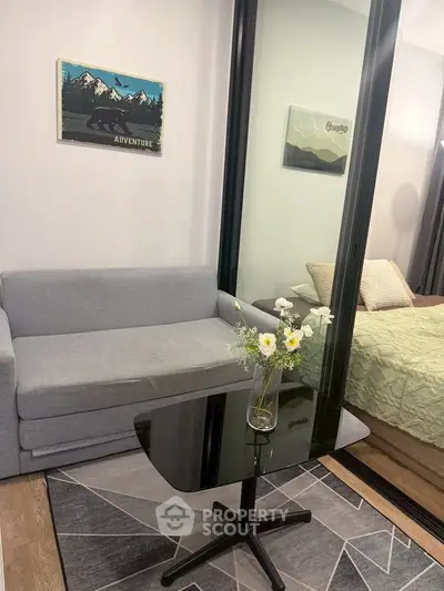 Modern living room with sleek glass table and cozy sofa, adjacent to a stylish bedroom.