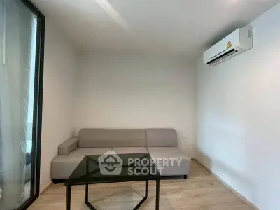 Modern minimalist living room with sleek sofa and glass coffee table, featuring air conditioning.